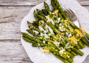 Green asparagus with a yellow sauce on a wooden background.